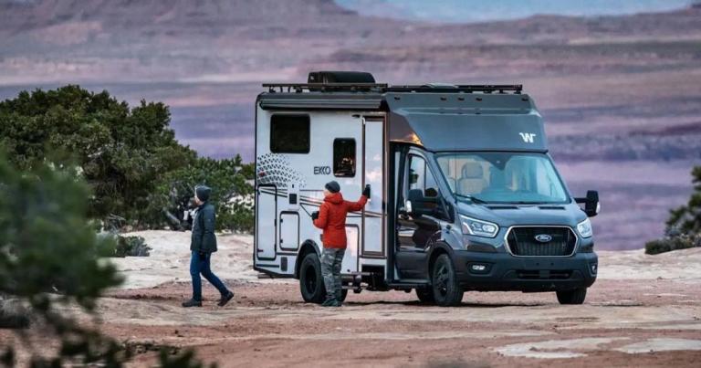 Class C RV parked outside with two people near it