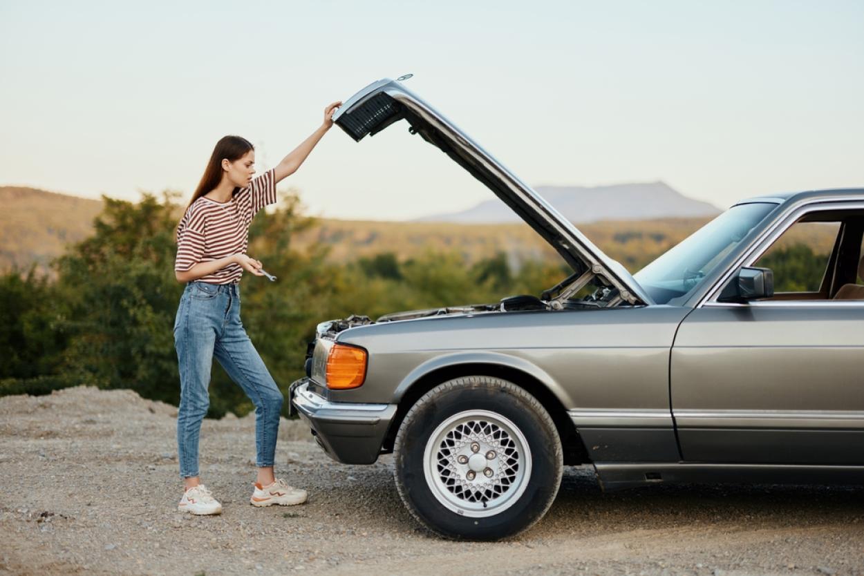 Person stands in front of a car with its hood up on the side of a desert road