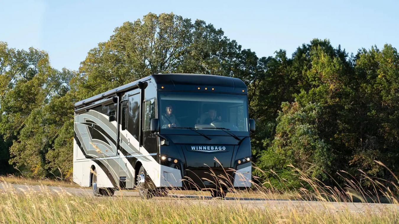 A front shot of a Winnebago RV driving along a forest