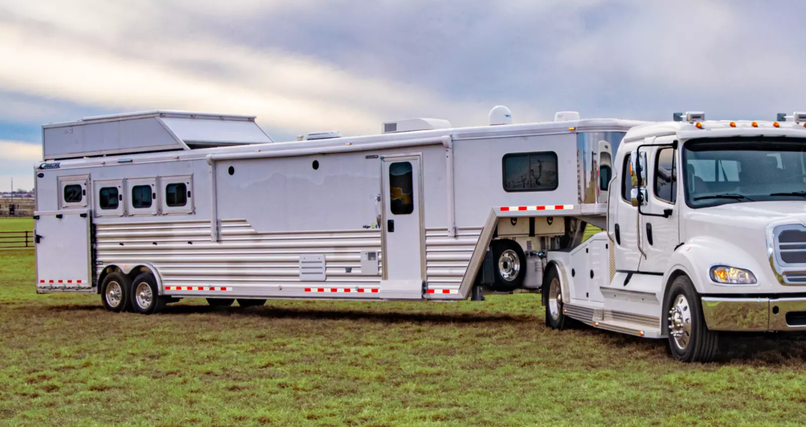 A white truck with a large white trailer attached in an open, grassy field