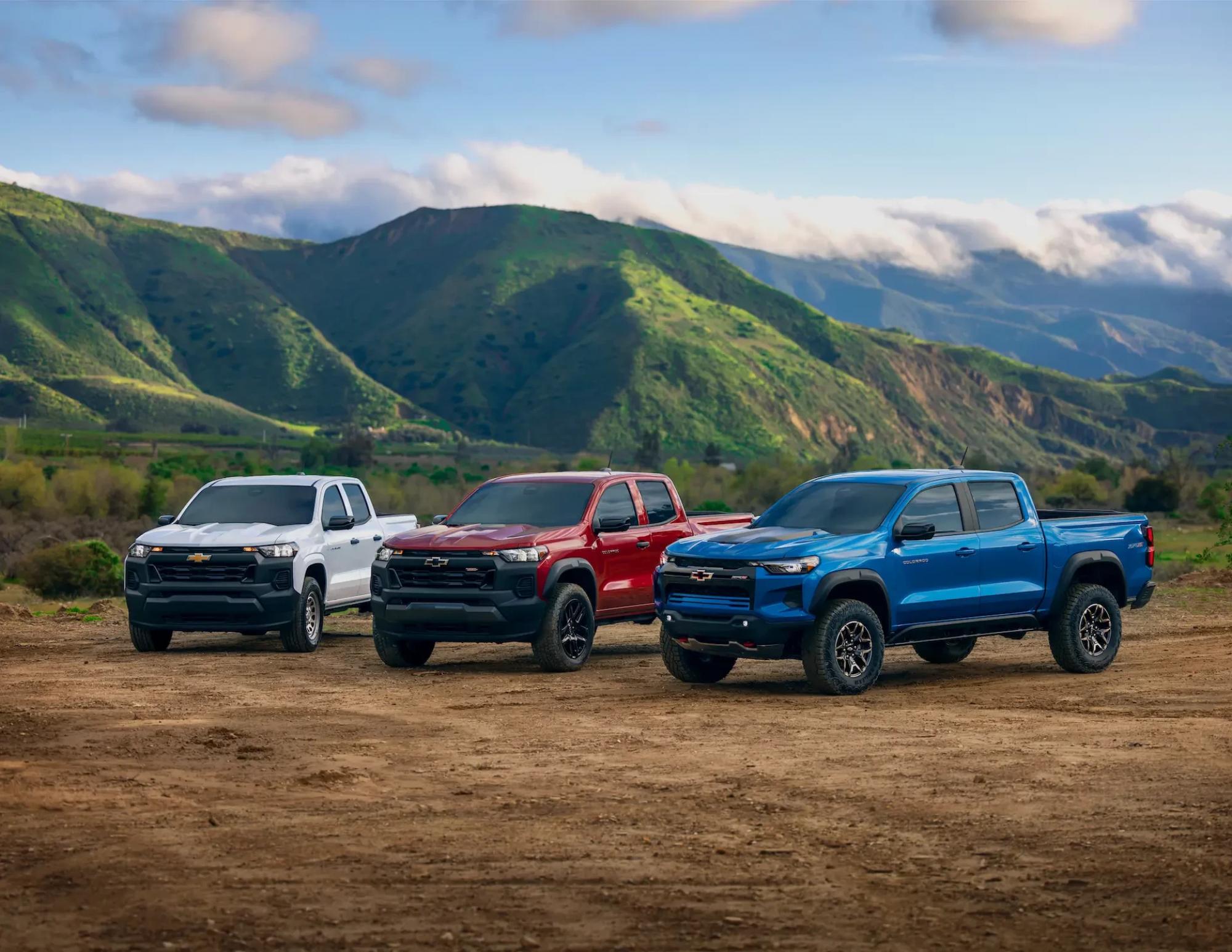Three Chevrolet pickup trucks, one white, one red and one blue, parked side by side off-road