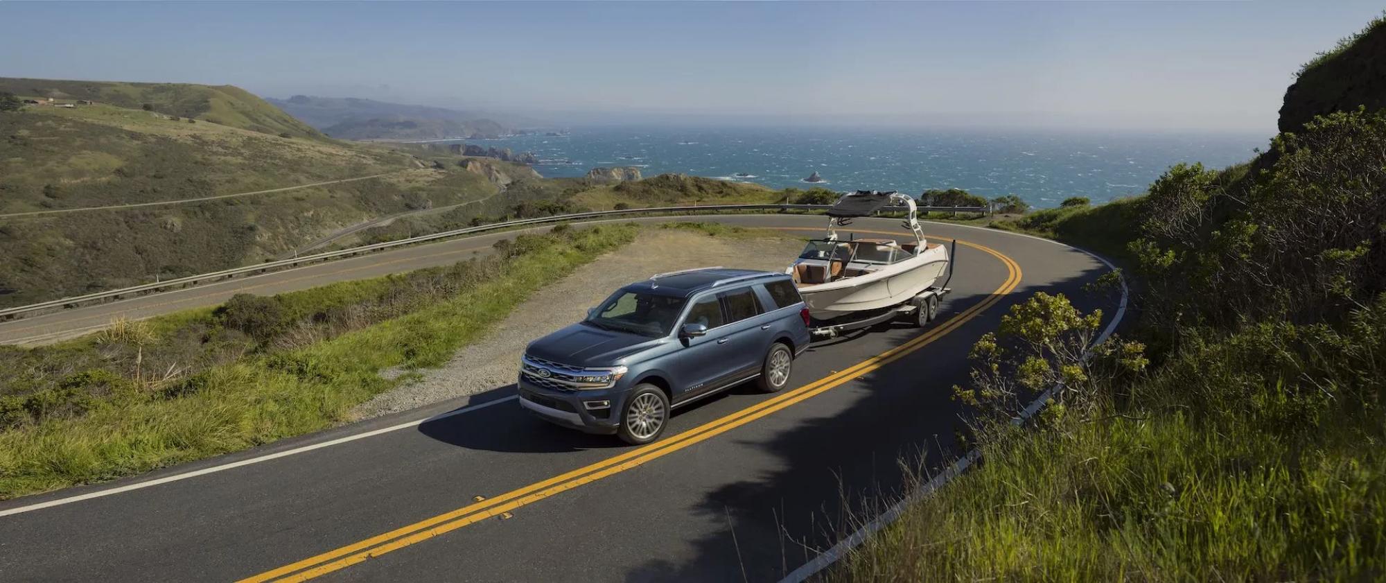 Grey Ford SUV towing a boat driving up a road overlooking the ocean