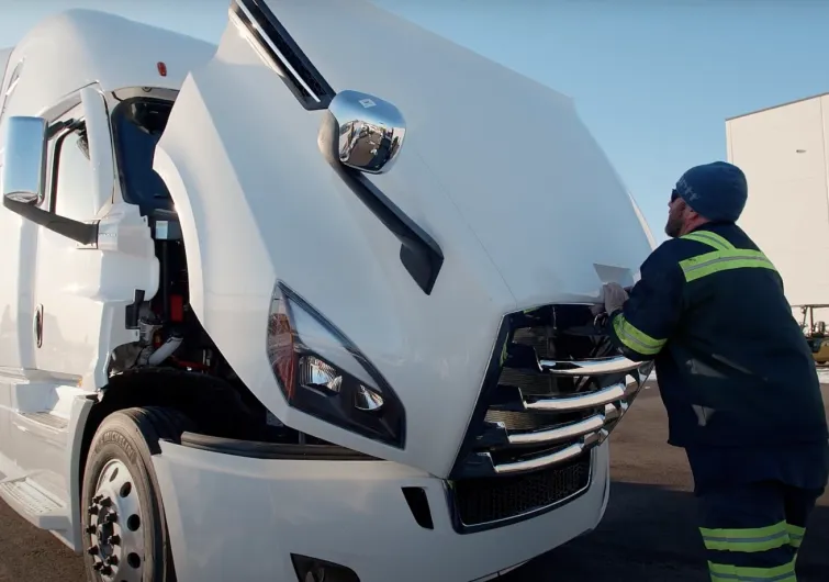 A man pushing down the hood of a commercial truck